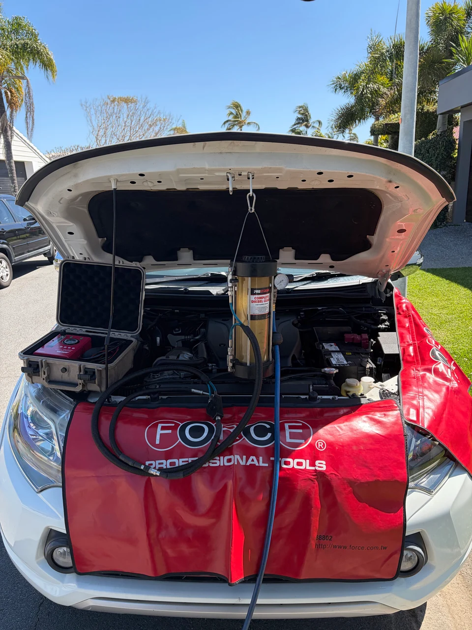 Diesel cleaning equipment and hoses connected under an open bonnet, with red protective covers over the front of the vehicle